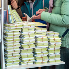 Young women and table with stack of books. Tall piles of various books stacked together in indoor store setting. Concept of books, literature abundance, choice overload and printed knowledge