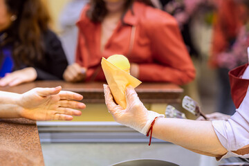 Ice cream seller giving ice cream cone to customer. Vendor in glove handing yellow ice cream cone to customer across counter. Concept of ice cream, food service, organic summer refreshment