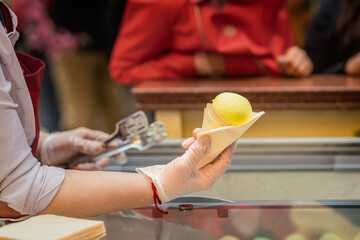Close-up of vendor holding yellow ice cream cone over counter in public place. Concept of ice cream, frozen product in summer, sweet craving, refreshment. Small business support