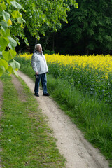 Elderly man with binoculars taking a relaxing stroll along a path next to a vibrant yellow canola field, embracing the beauty of nature in poland