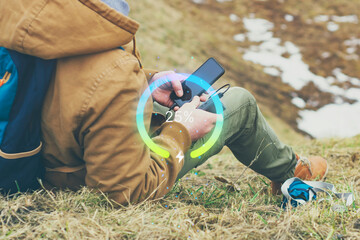 A traveler in the mountains charges his Smartphone with portable Power Bank. The battery indicator shows the percentage of charge. The concept of travel and outdoor chargers.