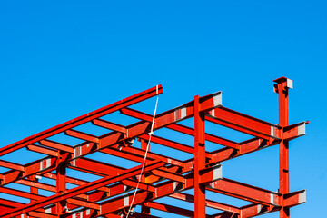 Red structural grid under blue sky, exposed steel framework in early stage construction with emphasis on geometry and repetition