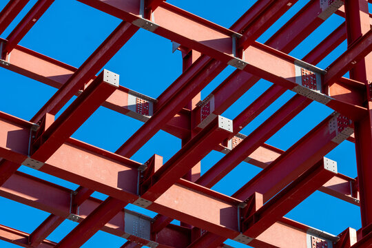 Intersecting steel beams with clean blue sky, abstract view of construction framework highlighting rhythm, repetition and structure