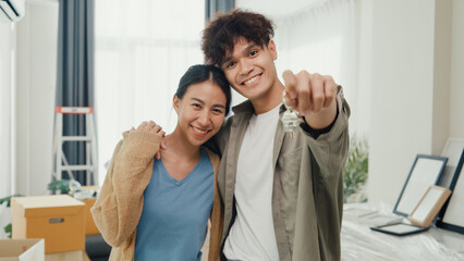 Young happy Asian sweet couple hugging each other smiling looking at camera show proud show off new house keychain in living room. Husband wife move new home, Apartment Rent And Ownership Concept.