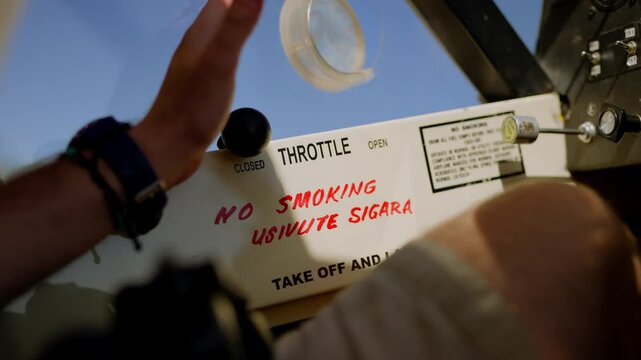 Close up of hand testing small light plane throttle with no smoking sign under it in English and Swahili languages on clear sky sunny day in Kenya