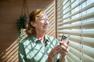 Senior woman smiling during a video call on smartphone at home in sunlight
