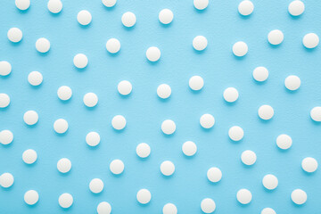 White pills on light blue table background. Pastel color. Closeup. Medicine pattern. Top down view.