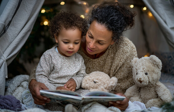 Mother reading a story to her toddler son in a blanket fort