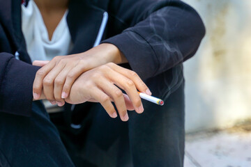 young man uses his hand to pick up a cigarette while sitting alone smoking. Soft and selective focus.