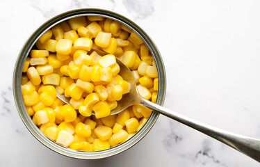 Top view of a spoon in a can of yellow corn with copy space. Food preservation concept. 