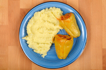 Top-down shot showcases two cooked stuffed bell peppers with a side of creamy mashed potatoes on a blue plate, served on a wooden surface
