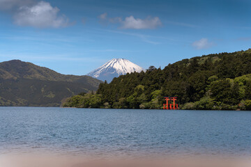 Mount Fuji with snow-capped peak seen behind Lake Ashi and the iconic red torii gate of Hakone...