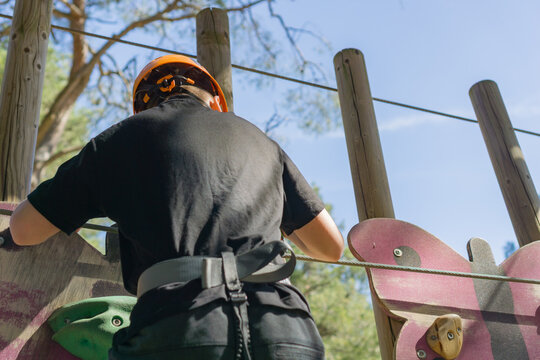 Boy in orange helmet on climbing wall, back view, navigating obstacle course, concept of adventure park, kids sports, outdoor challenge