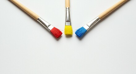 Obraz premium Three paintbrushes with primary colors (red, yellow, and blue) placed on a clean white surface