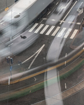 Long exposure photograph of a busy city intersection from above, capturing the motion blur of cars and trams in dynamic streaks of light and color.