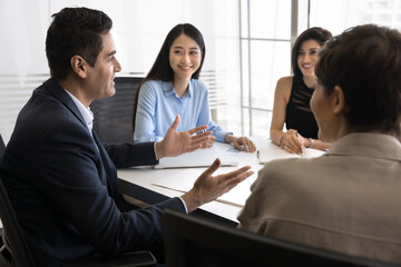 Mature Indian boss hold briefing seated at table in conference room, setting corporate goals, motivate young team, share strategy, provide project details, leading negotiation with investors in office