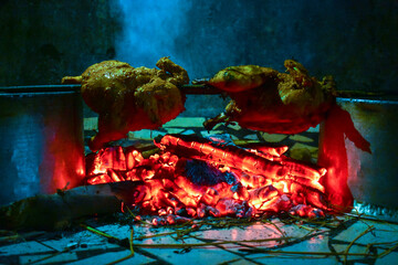 Two chickens roast over glowing embers on a spit.