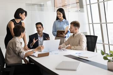 Multiethnic employees listening middle-aged Indian male boss during group meeting in modern...