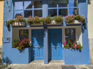 Blue building facade with flower boxes. Travel to Valencia, Spain. Blue wooden door decorated with flowers. Ideas for window decoration