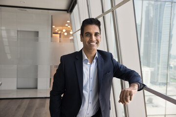 Portrait of confident mature Indian businessman, company owner or executive manager, standing near...