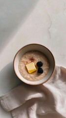 Bowl of millet porridge topped with butter and blackberries on table  