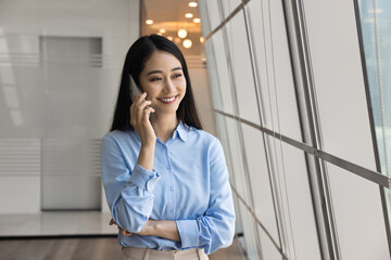Chinese businesswoman engaged in formal conversation with client on mobile phone, smiling,...