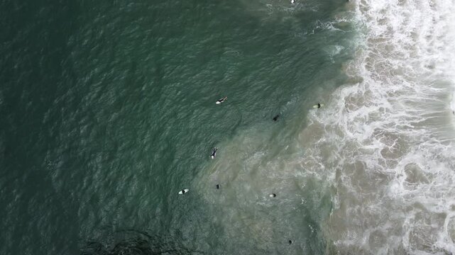 Aerial view of surfers catching waves near Manhattan Beach Pier under moody skies—California’s coast in motion from above.