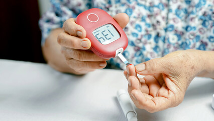 Fototapeta premium Elderly person checking blood sugar level with digital glucose meter, close up of hands, diabetes management, healthcare and medical concept, home monitoring, floral shirt visible