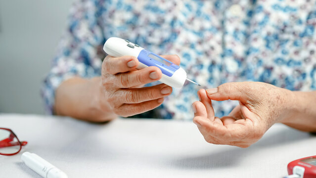 Elderly person using blood glucose meter for diabetes management, sitting at table with medical device, focusing on health care and self monitoring at home