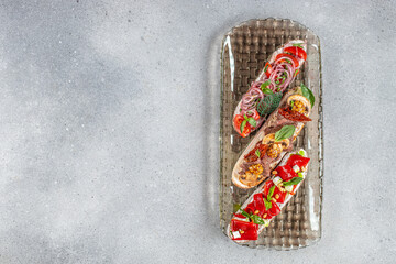 Gourmet bruschetta trio with fresh toppings including vegetables, herbs, meat, and cheese served on a textured glass platter over a stone surface