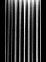 Obraz premium Striking interplay of light and shadow on a vertically ribbed surface, creating a sleek and modern abstract design in black and white.