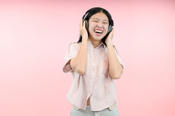 young asian woman enjoy hearing music from headphone in studio pink background