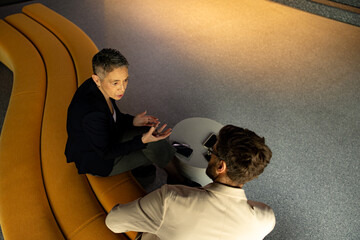 Two businesspeople engaging in discussion while seated on a stylish yellow sofa in a modern office lobby, fostering collaboration and teamwork