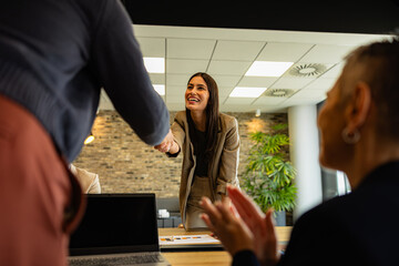 Businesswomen shaking hands after closing a deal while colleagues are clapping, celebrating success in modern office