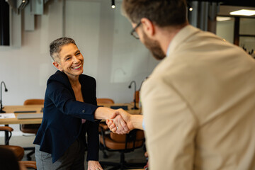 Businesswoman and businessman shaking hands in a modern office, both smiling while finalizing a successful deal and partnership