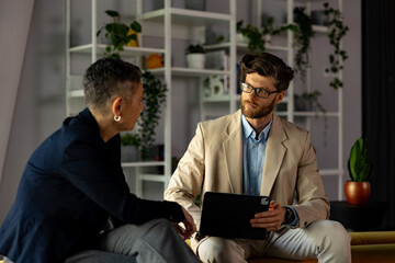 Businessman presenting a project on a tablet while engaging in discussion with a businesswoman in a modern office setting