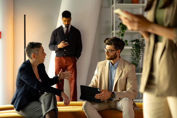 Businesspeople engaging in discussion while using digital devices in a modern office setting during a collaborative meeting