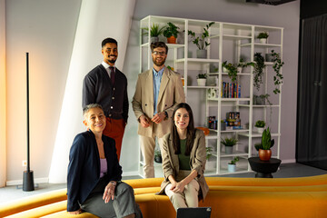 Four startup businesspeople posing together in a bright, modern office, surrounded by greenery and a stylish white bookshelf