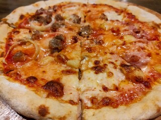 A close-up of a freshly baked pizza with melted cheese, pepperoni, sausage, and onion on a wooden table.