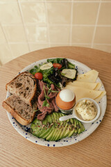 Sandwich with meat, avocado, egg and with freshly greens. Crop delicious breakfast served on wooden table in sunny indoor cafe. Part of a series