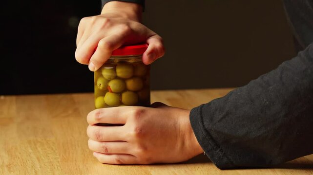 A woman is trying to open a jar of pickle olives with pimento