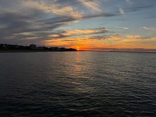 Fototapeta premium Sunset over calm ocean waters in the Ocean View area of Norfolk, Virginia with shoreline homes and a golden sky
