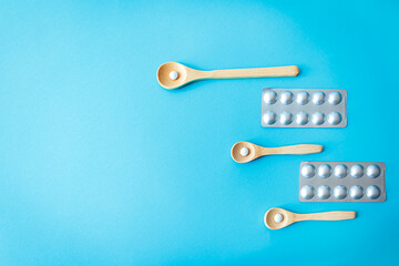 White pills on wooden spoons with blister packs on blue background. Flat lay combining natural and pharmaceutical health concepts, treatment and supplement routine