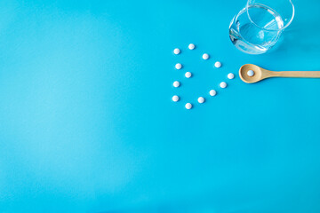 Minimalist flat lay with pills forming a heart, wooden spoon, and glass of water. Health and wellness concept with copy space