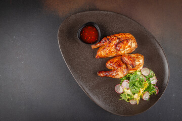 Roasted cornish hen with fresh green salad, radish slices, and spicy red sauce. top view. copy space