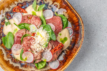 Beef carpaccio with radish, spinach, parmesan, dried tomatoes, and creamy dressing. top view. copy space