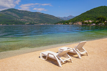 Beautiful sunny Mediterranean landscape. Montenegro, Adriatic Sea. View of Bay of Kotor near Tivat city. Two  chaise-longues on sand beach