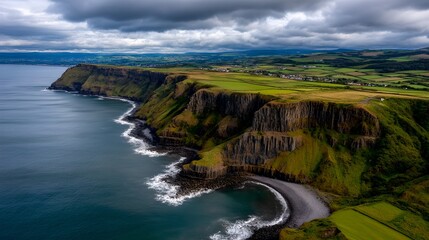 Obraz premium Dramatic Aerial View of Coastal Cliffs Green Fields and Ocean Waves