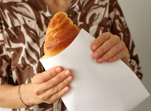 Woman's hand hold a fresh whole croissant. Closeup on croissants with butter in french pastry shop.