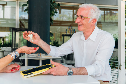 Professional real estate agent handing over house keys to client after signing property contract on digital tablet, finalizing real estate transaction - Powered by Adobe